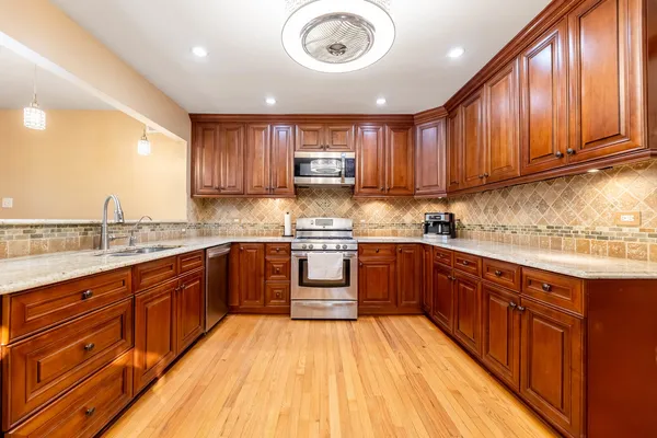 a kitchen with stainless steel appliances granite countertop wooden cabinets a sink and dishwasher a stove with wooden floor
