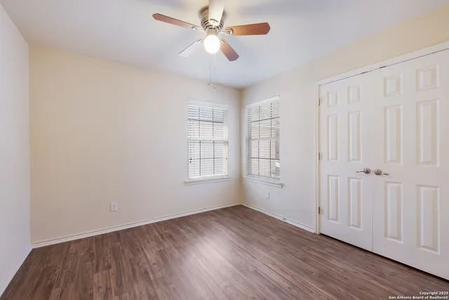 an empty room with wooden floor chandelier fan and windows