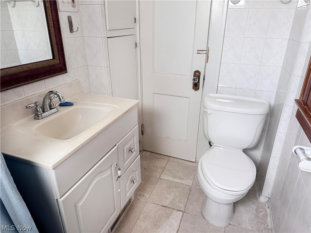 7121 North Lima Road Youngstown, OH 44514 - Photo 26 of 37 Bathroom featuring a vanity with an integrated sink and chrome faucet, white toilet, tiled walls, and light-toned floor tiles