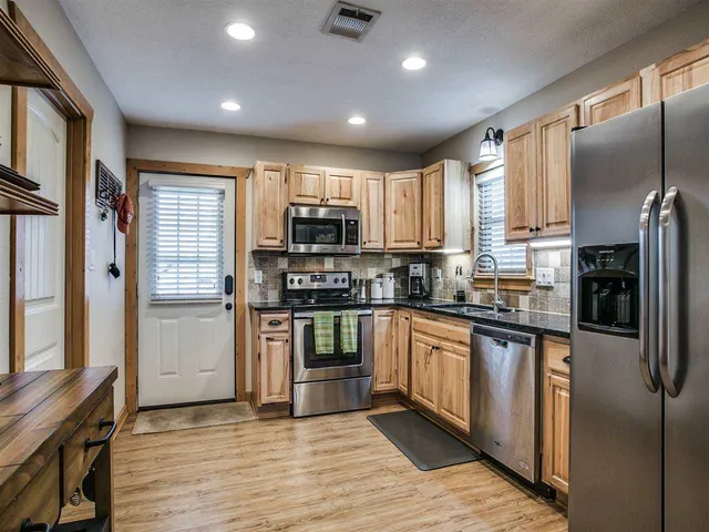 a kitchen with stainless steel appliances granite countertop a refrigerator a stove top oven a sink and dishwasher with wooden floor