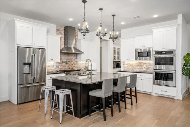 a kitchen with stainless steel appliances granite countertop a refrigerator a sink dishwasher a stove and a dining table with wooden floor