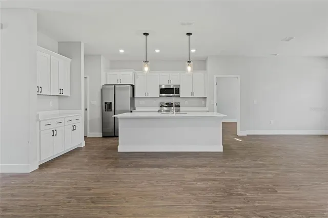 a large kitchen with stainless steel appliances granite countertop a stove a sink and white cabinets with wooden floor