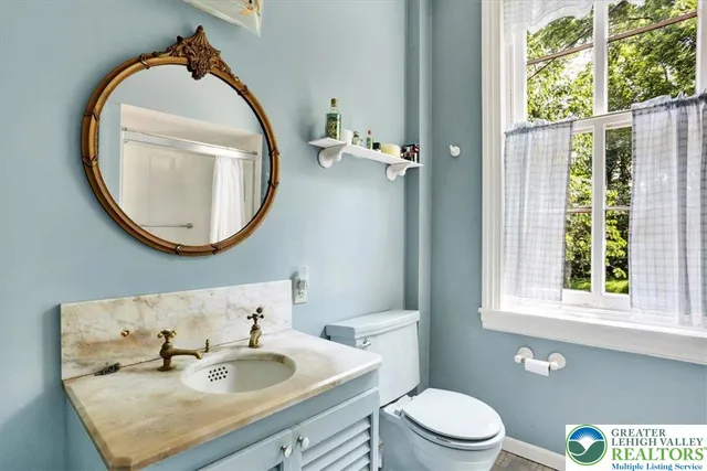 a bathroom with a granite countertop sink toilet a large mirror next to a window