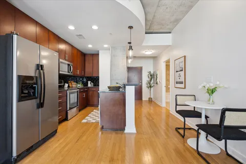 a kitchen with stainless steel appliances kitchen island granite countertop a refrigerator a stove top oven and a dining table with wooden floor