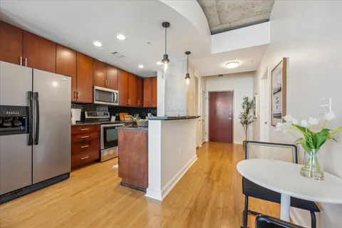 a kitchen with stainless steel appliances kitchen island granite countertop a refrigerator a stove top oven and a dining table with wooden floor