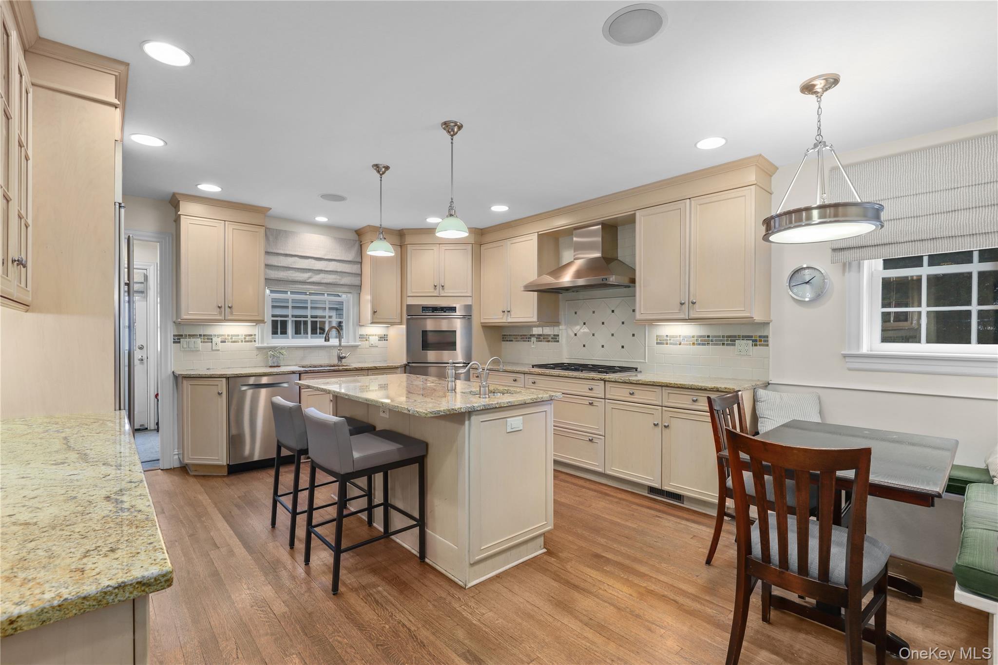 12 Sunnybrae Place Bronxville, NY 10708 - Photo 8 of 40 Eat-in Kitchen with a breakfast bar area, decorative light fixtures, light stone countertops, light wood finished floors, and wall chimney range hood