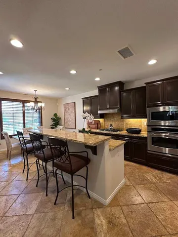 a kitchen with stainless steel appliances granite countertop a table chairs sink and cabinets