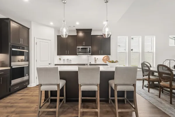 a kitchen with stainless steel appliances kitchen island granite countertop a dining table chairs and a refrigerator