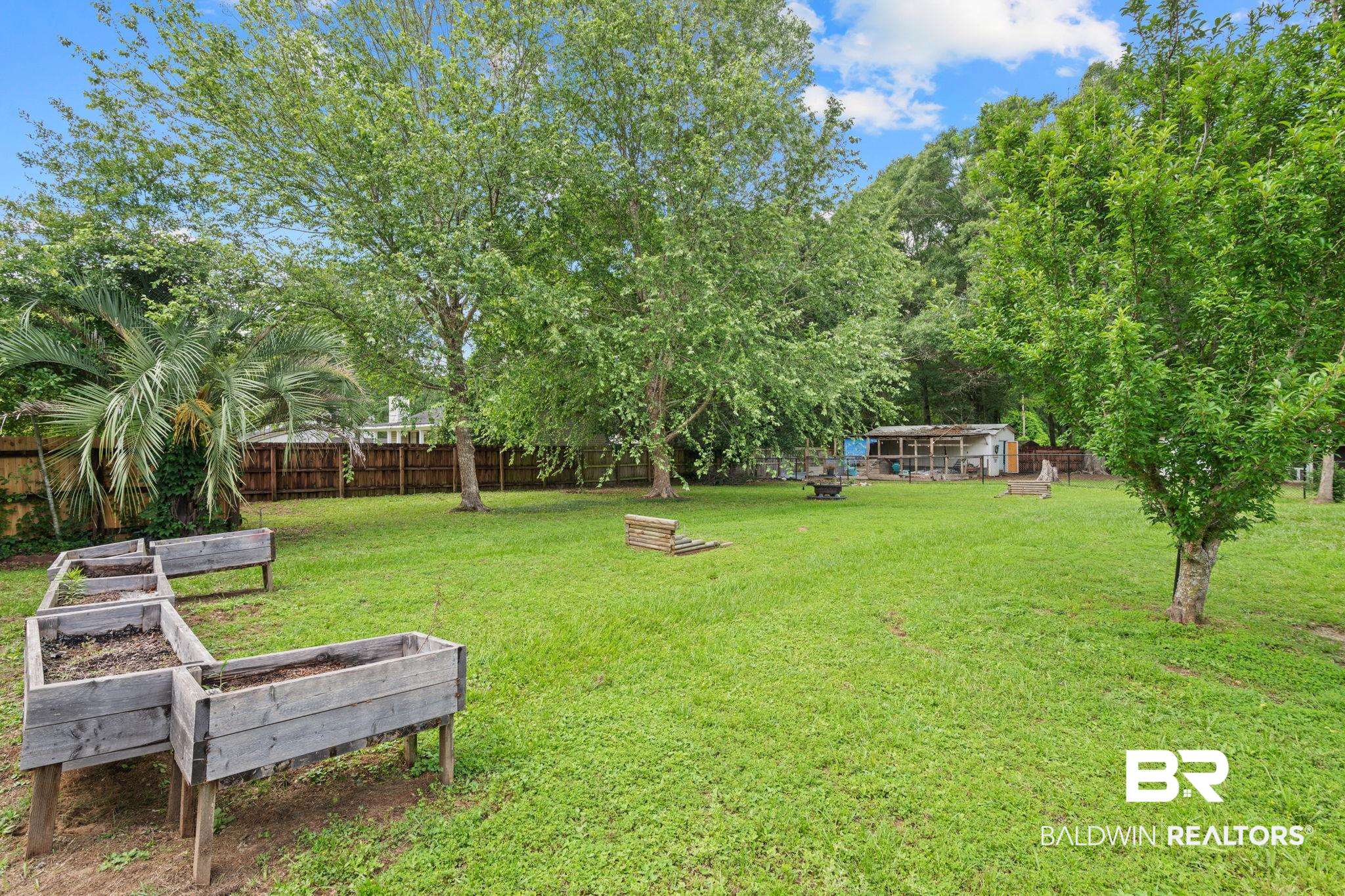 5936 Lundy Road Theodore, AL 36582 - Photo 30 of 32 Expansive grassy yard featuring mature trees, a privacy fence, and multiple raised garden beds