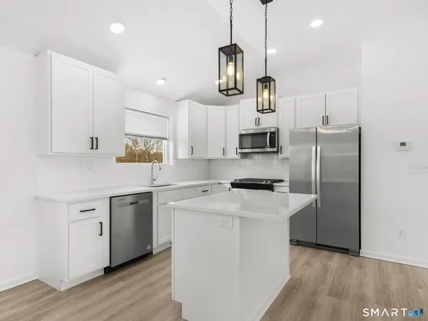 a kitchen with stainless steel appliances granite countertop white cabinets a refrigerator a sink a stove and a wooden floors