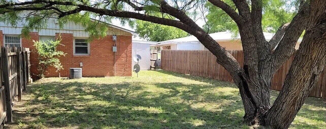 4427 31st Street, Unit A Lubbock, TX 79410 - Photo 9 of 9 a backyard of a house with large trees and a barn in the background