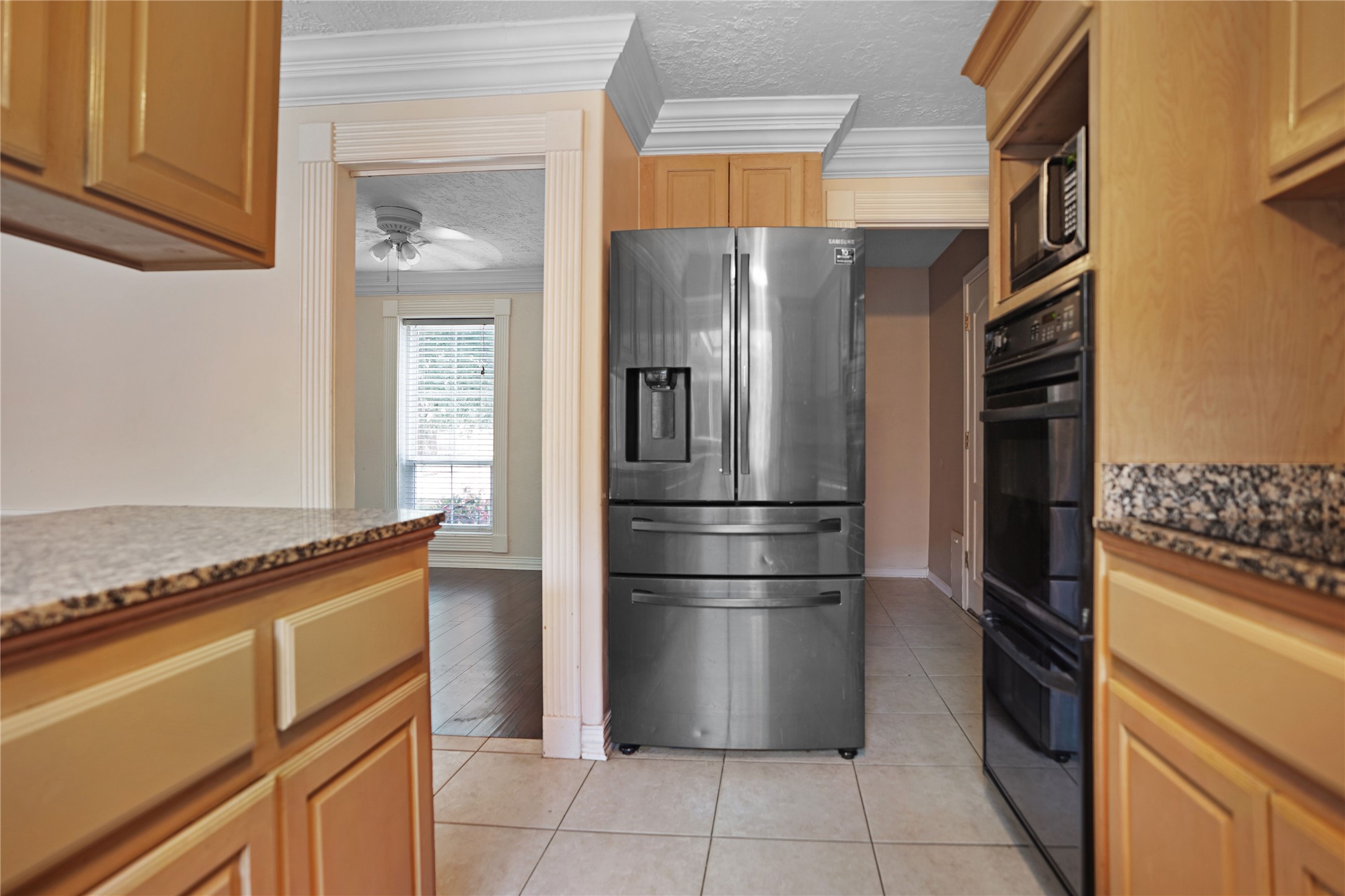 17119 Mellow Ridge Drive Spring, TX 77379 - Photo 10 of 32 This kitchen features stainless steel appliances, including a modern refrigerator and double oven. It has granite countertops, tile flooring, and a view into a bright room with wooden floors and a ceiling fan.