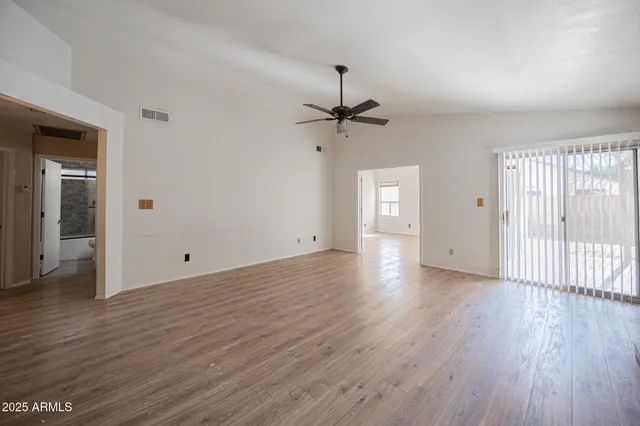 an empty room with wooden floor fan and windows