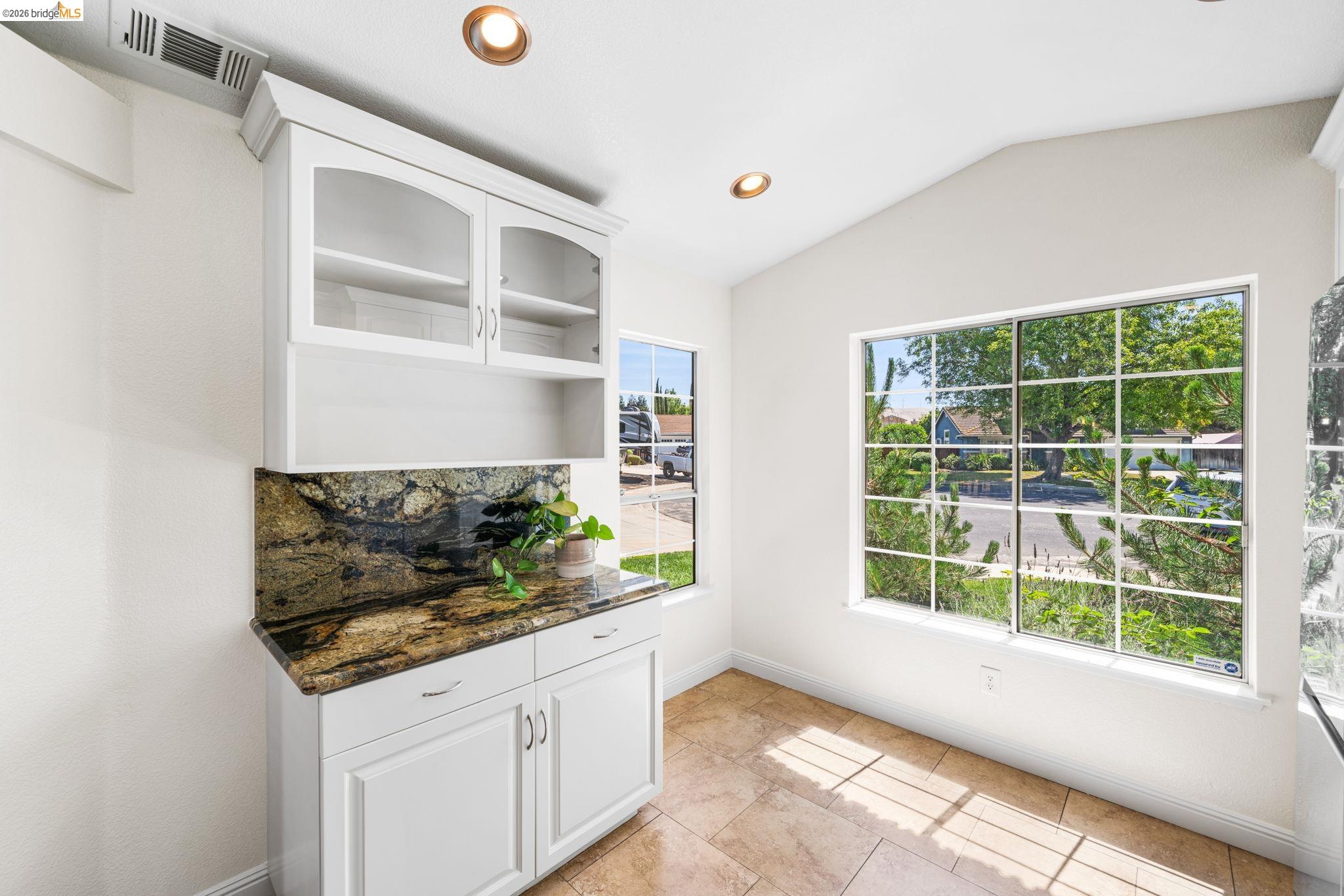 1186 El Rio Court Livermore, CA 94551 - Photo 17 of 60 Custom built-in cabinetry with glass-front uppers, a patterned stone countertop, and matching stone backsplash