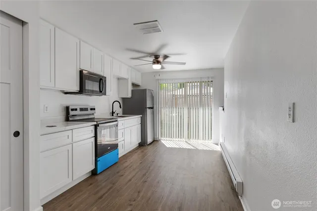 a kitchen with stainless steel appliances white cabinets a sink a stove a refrigerator with a dining table and chairs