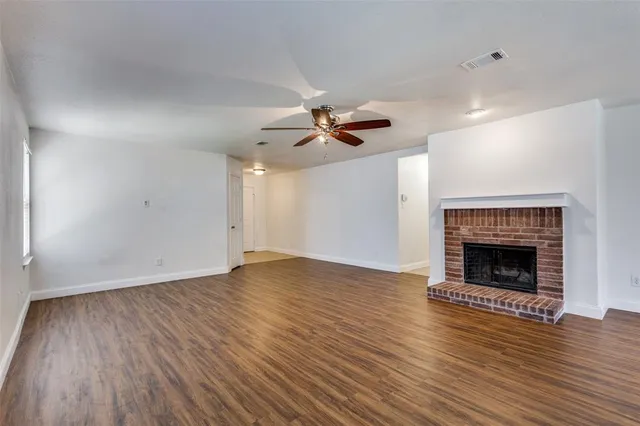 a view of an empty room with wooden floor fireplace and a window