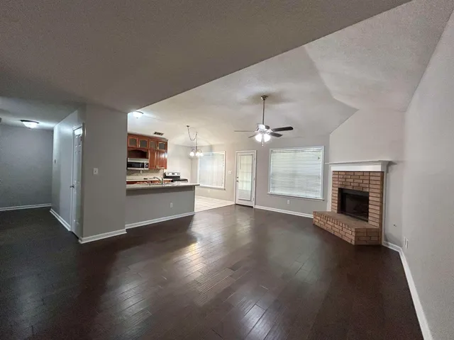 an empty room with wooden floor fireplace and kitchen view