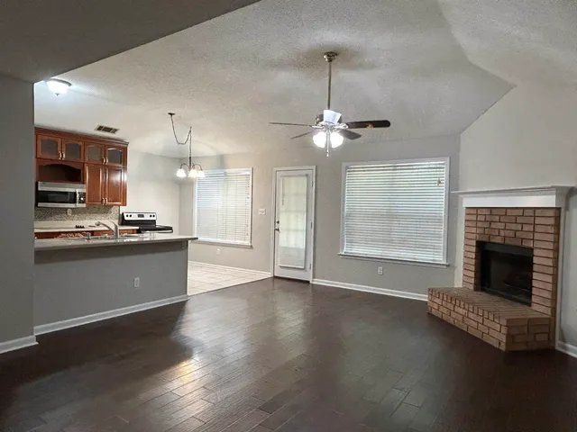 a view of an empty room with kitchen and fireplace