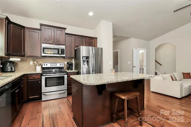 a kitchen with stainless steel appliances granite countertop a stove a sink dishwasher a refrigerator and a oven with wooden floor