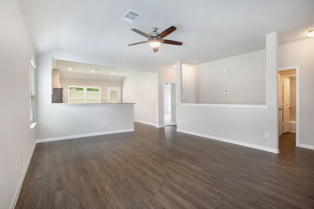 a view of an empty room with wooden floor and a ceiling fan
