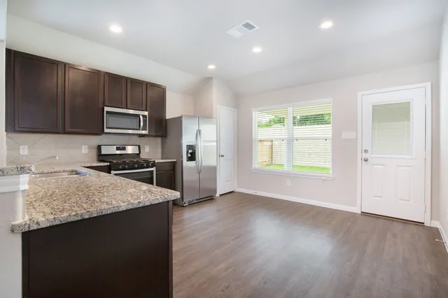 a kitchen with stainless steel appliances granite countertop a stove a sink and a refrigerator with wooden floors