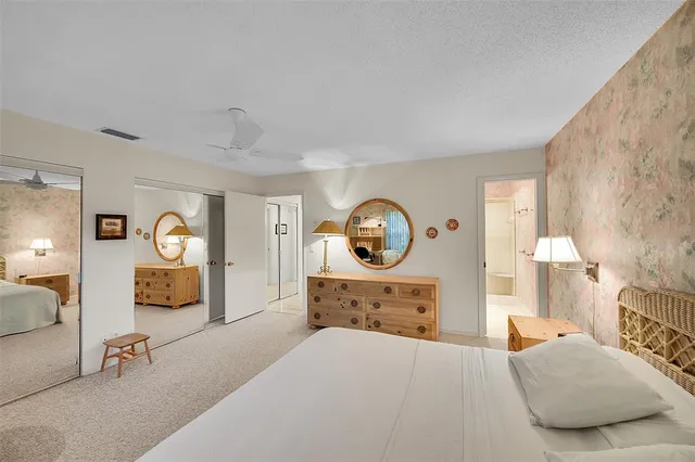 a bedroom with a bed and a lamp on dresser next to a large window