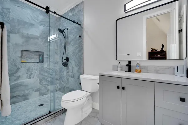 a bathroom with a toilet a sink a glass door a shower and mirror