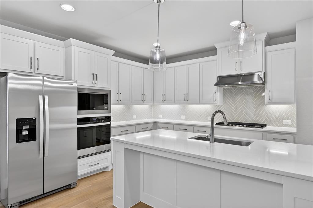 4123 Windy Point Court Oak Point, TX 75068 - Photo 14 of 29 Kitchen featuring a central island with an undermount sink, pendant lighting, stainless steel appliances, white cabinetry, and a herringbone tile backsplash