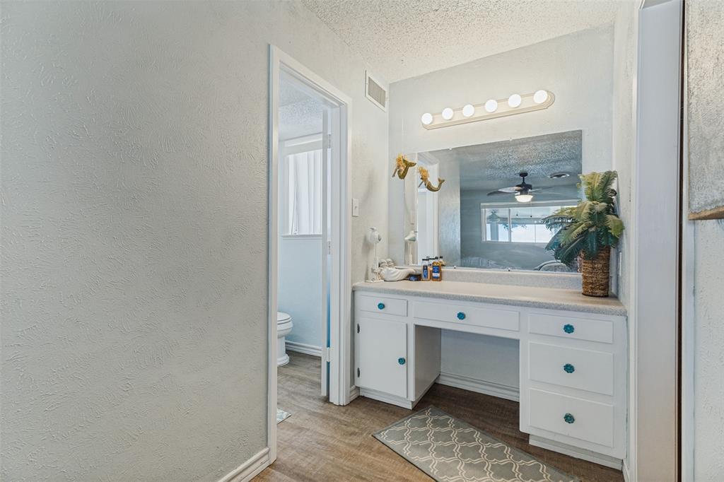 12960 Gantt Road East Azle, TX 76020 - Photo 12 of 26 Built-in vanity with white cabinetry, countertop, and a large wall-mounted mirror with overhead lighting