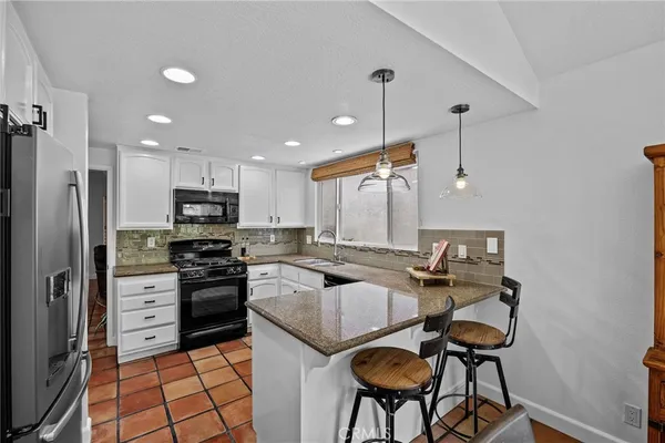 a kitchen with stainless steel appliances granite countertop a stove top oven a refrigerator a sink and a chairs