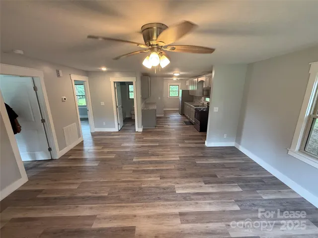 a view of a hallway with a big room with wooden floor and a ceiling fan
