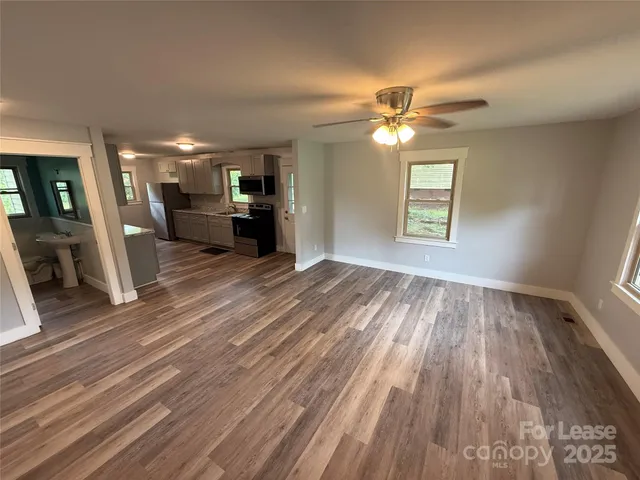 a view of a livingroom with wooden floor a ceiling fan and windows