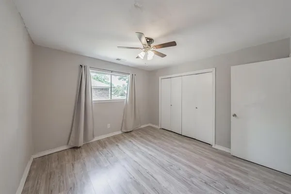 an empty room with wooden floor ceiling fan and windows
