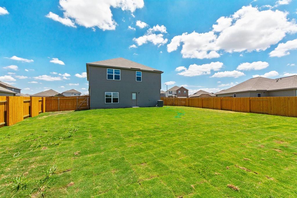 16429 Farmhouse Lane Elgin, TX 78621 - Photo 22 of 22 Expansive backyard featuring a manicured lawn, full perimeter wood fencing, and a two-story gray siding exterior