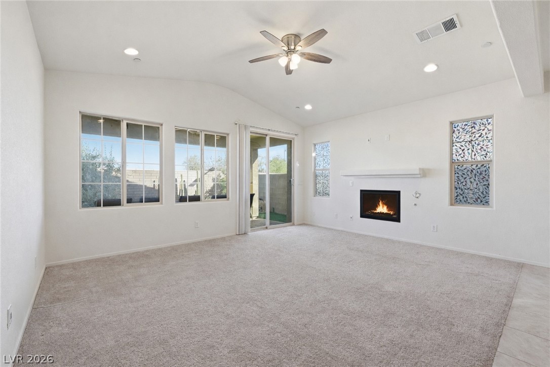 250 Dedication Avenue Henderson, NV 89011 - Photo 11 of 67 Unfurnished living room with a warm lit fireplace, a ceiling fan, vaulted ceiling, recessed lighting, and light colored carpet