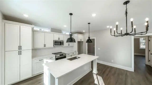 a kitchen with stainless steel appliances kitchen island granite countertop a refrigerator a stove and white cabinets with wooden floor