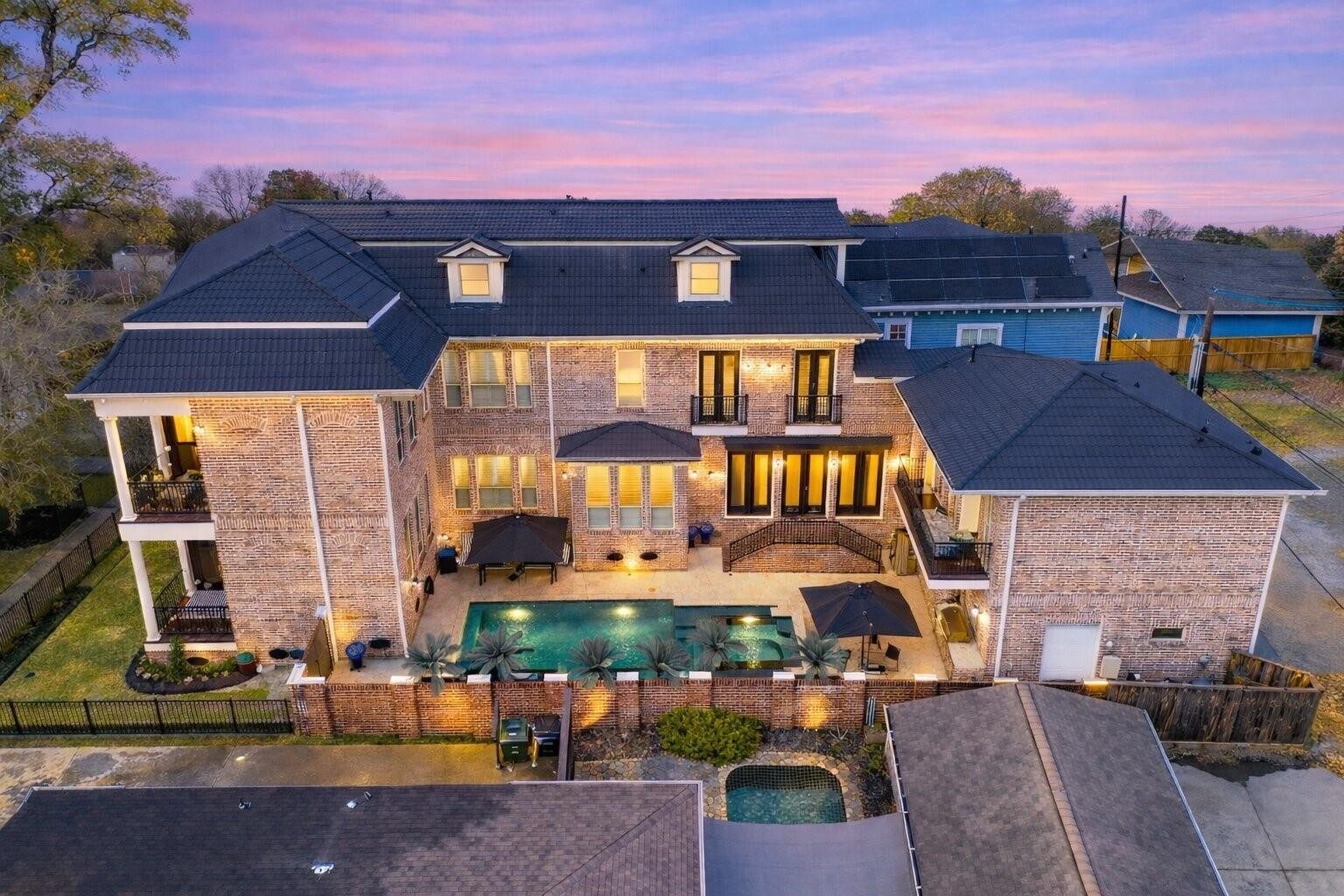 1418 Columbia Street Houston, TX 77008 - Photo 44 of 45 A striking all-brick residence designed for living at scale, glowing at sunset with balconies overlooking the pool, multiple outdoor spaces, a rare three-car garage with alley access, and a custom black metal shingle roof (2025) for lasting style and durability.