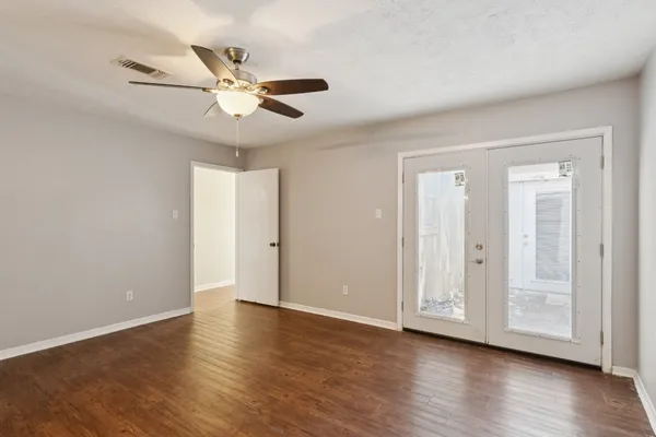a view of an empty room with wooden floor and a ceiling fan