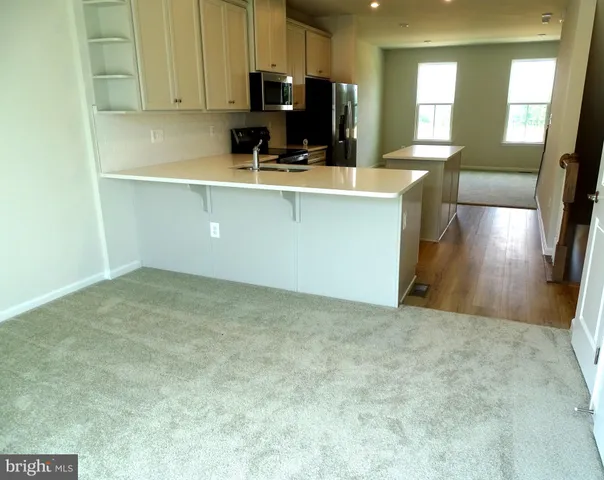 a view of a kitchen with kitchen island a sink wooden floor and a view of living room