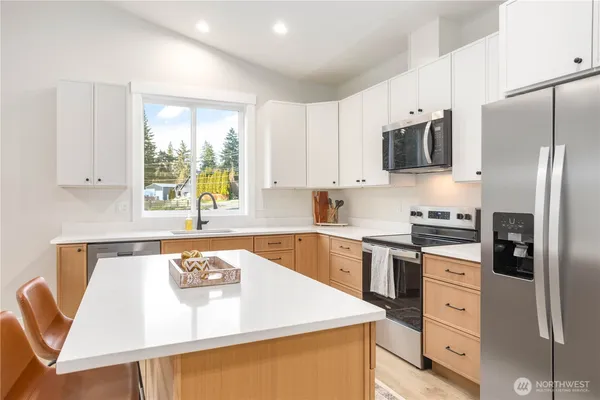 a kitchen with stainless steel appliances granite countertop a sink a stove a refrigerator with white cabinets and wooden floor