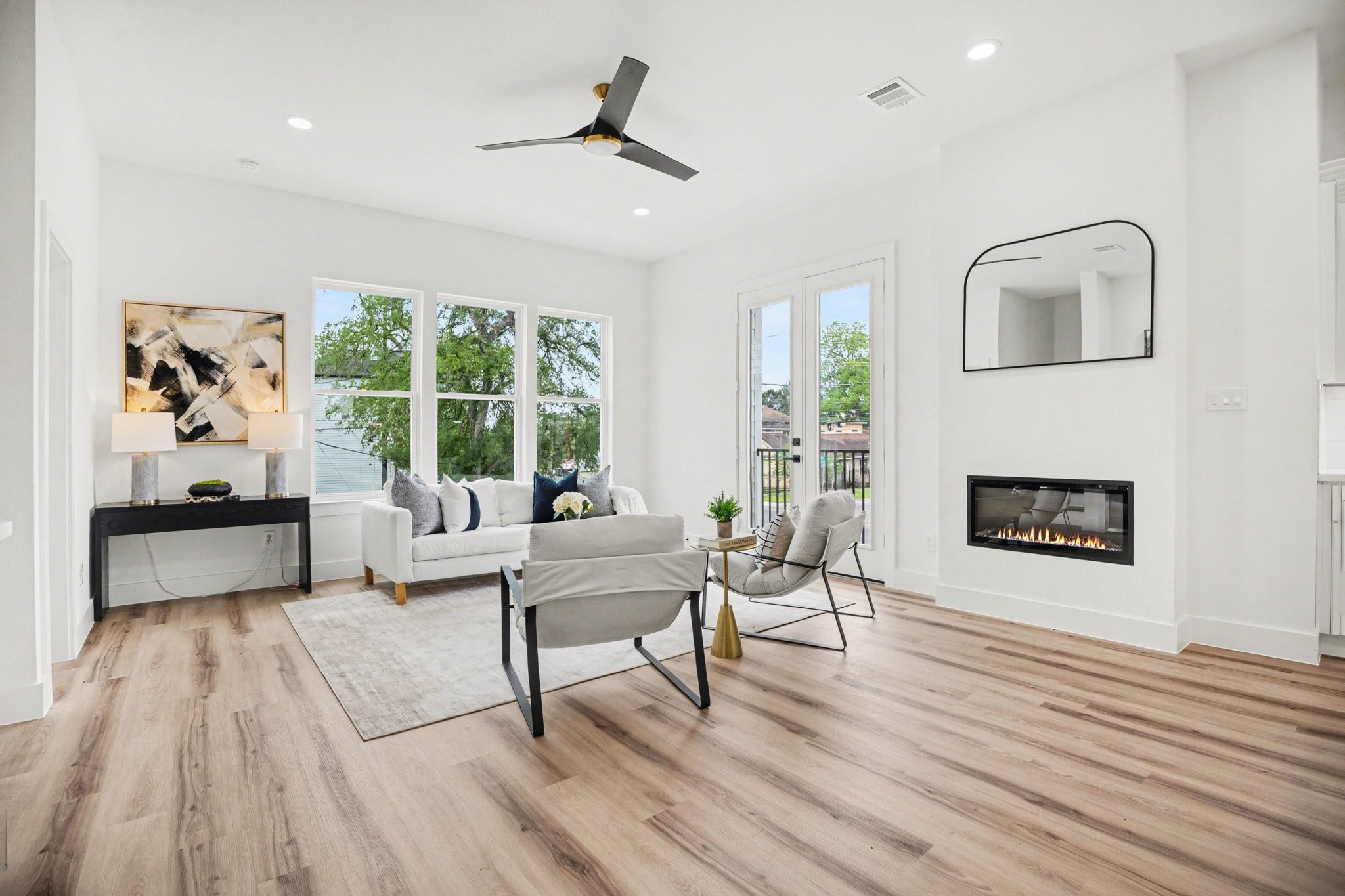 115 Milby Street Houston, TX 77003 - Photo 5 of 28 Bright and modern living room with large windows, sleek wood flooring, and a cozy fireplace. It features contemporary furniture, a stylish ceiling fan, and a large wall mirror, creating an inviting and spacious atmosphere.