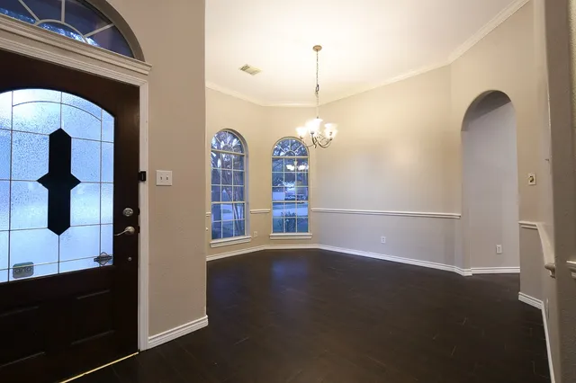 a view of an empty room with chandelier fan and wooden floor