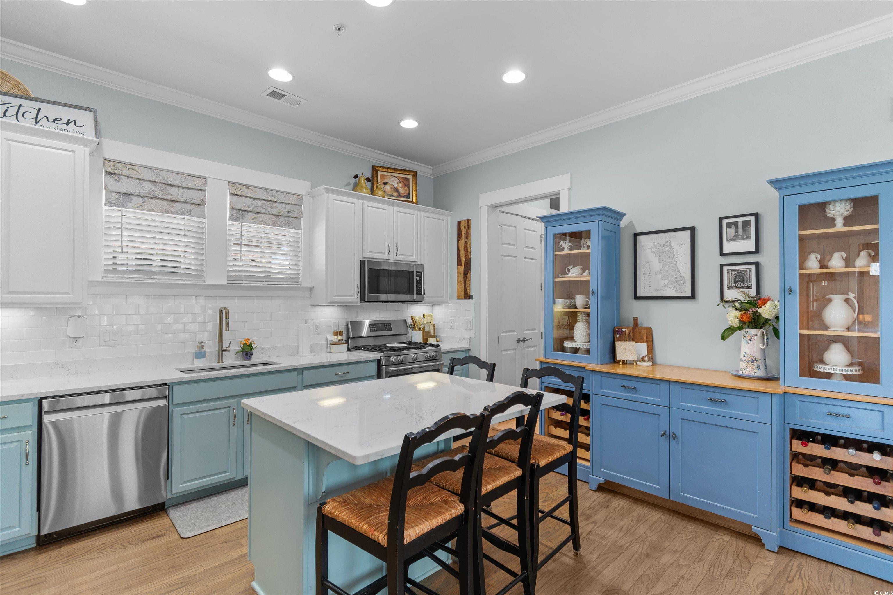 3448 Baldwin Lane Myrtle Beach, SC 29577 - Photo 3 of 30 Kitchen with blue cabinets, crown molding, appliances with stainless steel finishes, light wood finished floors, and tasteful backsplash