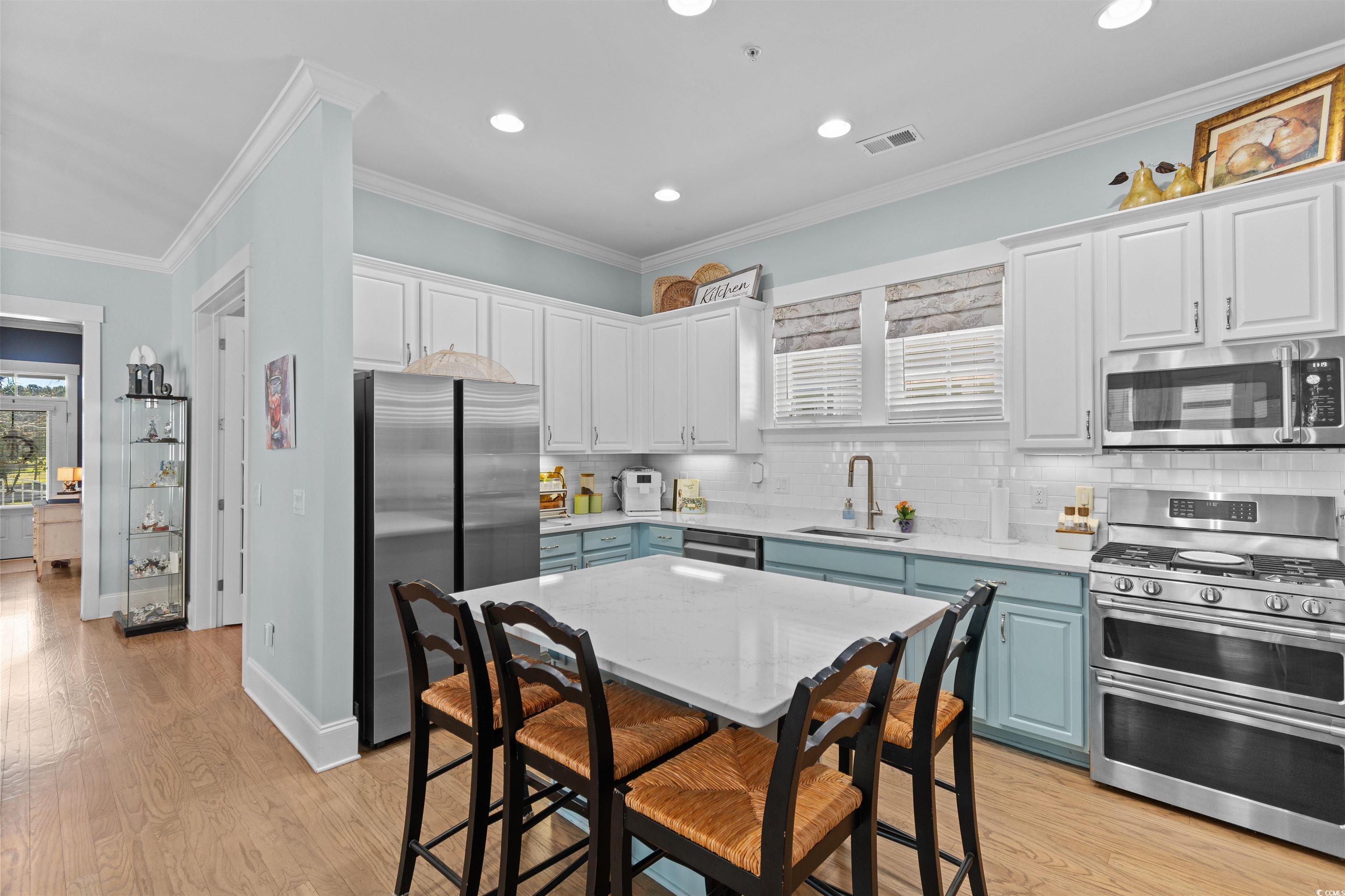 3448 Baldwin Lane Myrtle Beach, SC 29577 - Photo 7 of 30 Kitchen featuring appliances with stainless steel finishes, ornamental molding, light wood-style floors, white cabinetry, and decorative backsplash