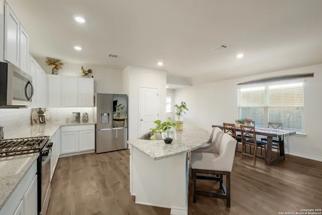 a kitchen with kitchen island a dining table chairs stainless steel appliances and cabinets