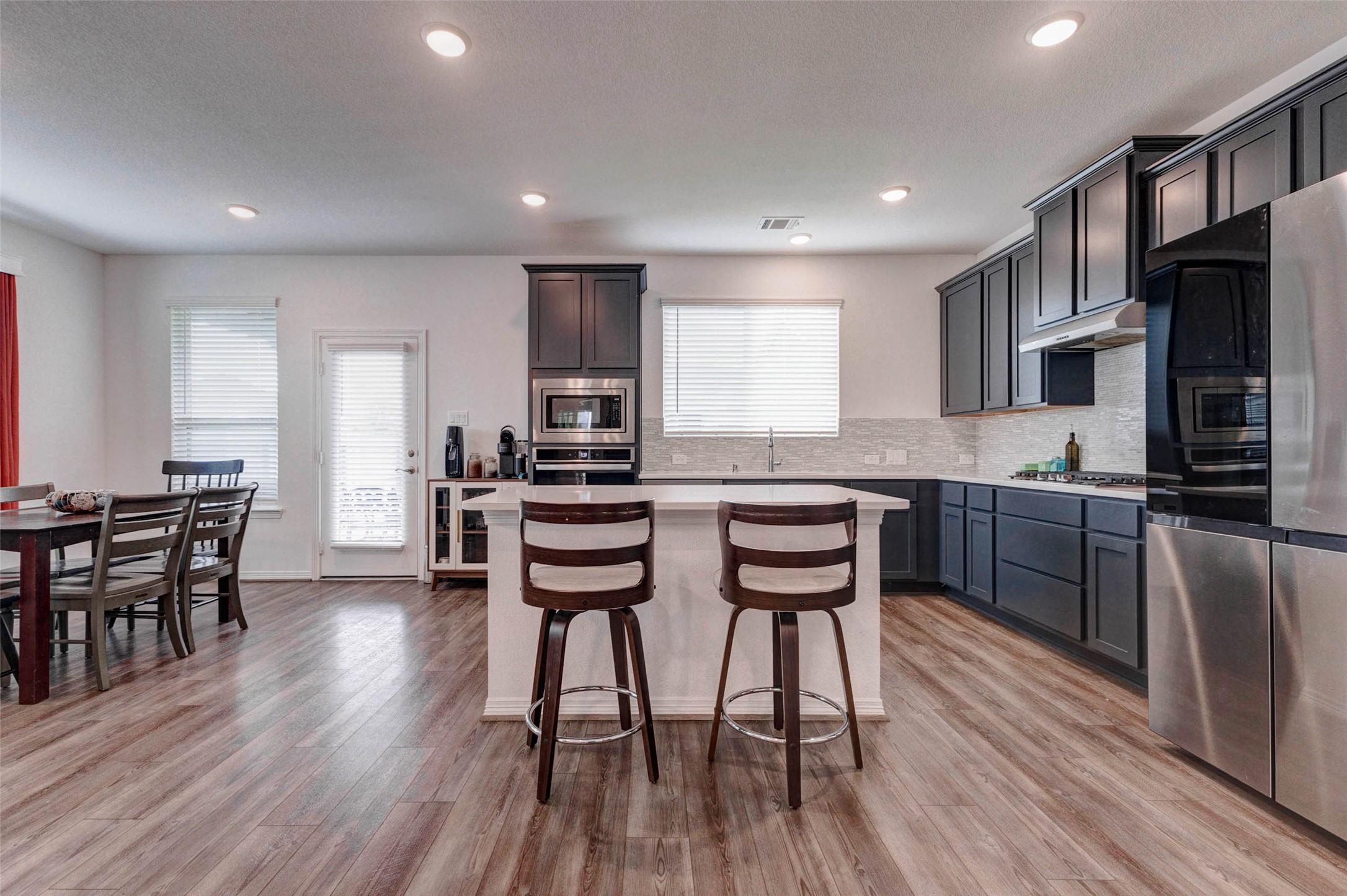 32418 Fly Fish Way Fulshear, TX 77441 - Photo 12 of 40 This angle of the kitchen beautifully illustrates just how functional and well-appointed the space truly is, with the island seating, full appliance suite, abundant cabinetry, and a dedicated dining area all flowing together effortlessly. The door off the kitchen provides convenient access to the backyard, making indoor and outdoor entertaining a natural extension of one another.