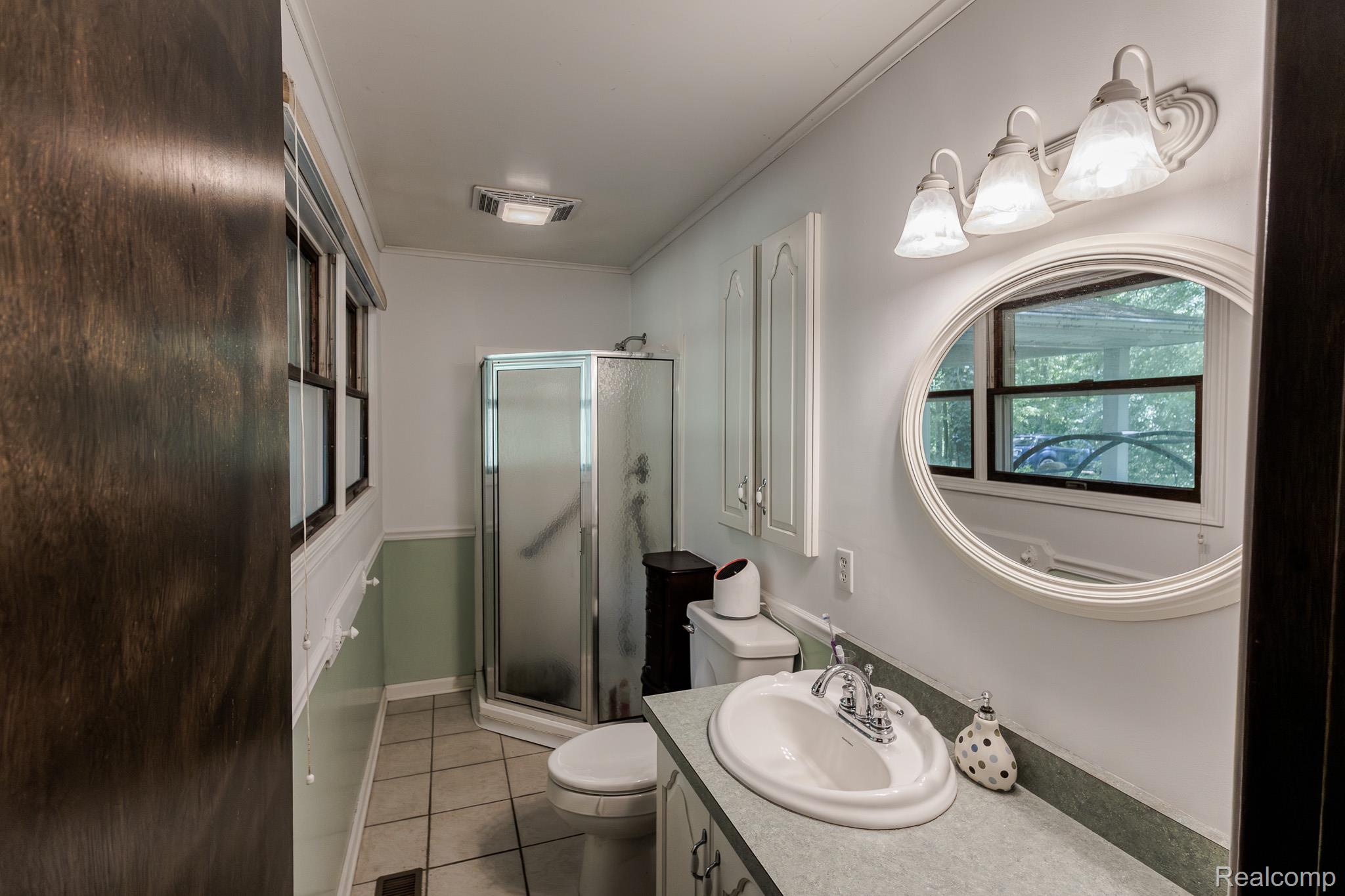 8197 Irish Road Millington, MI 48746 - Photo 26 of 38 Bathroom featuring a glass-enclosed shower, white vanity with an oval sink, oval framed mirror, and a three-light fixture