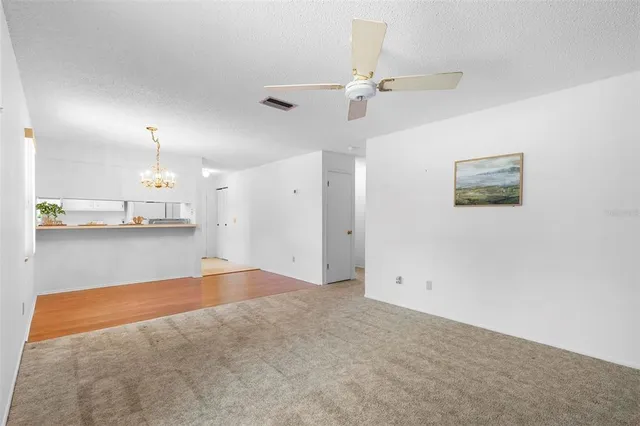 an empty room with kitchen view and a chandelier fan