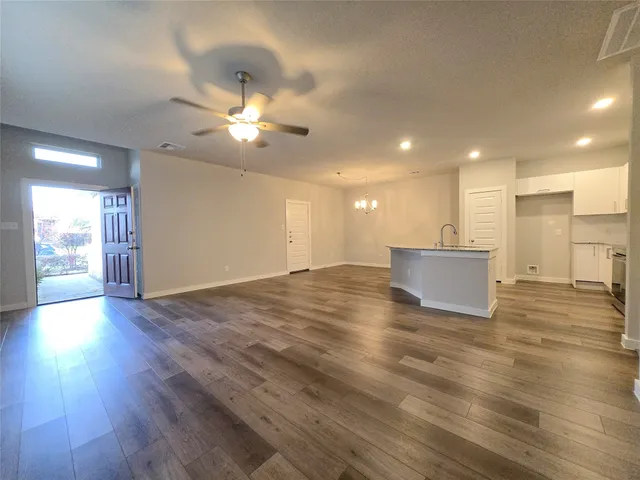 a view of an empty room with wooden floor and a ceiling fan