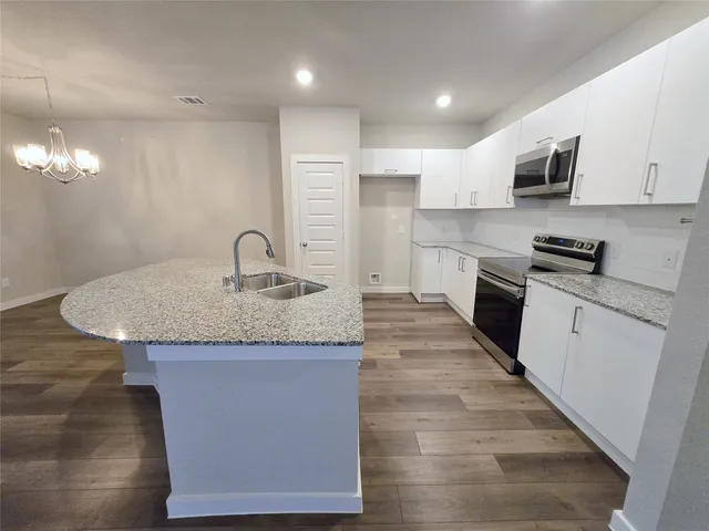 a kitchen with kitchen island granite countertop a stove top oven a sink a counter space and cabinets